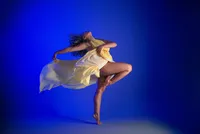 Dancer on pointe in a yellow costume against a vivid blue background, fabric caught mid-motion.