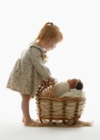 Toddler in a floral dress peeking at her newborn sibling in a basket prop during an Atlanta newborn photoshoot.