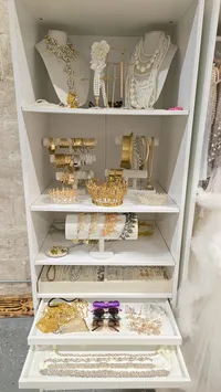 White accessory cabinet displaying statement necklaces, bracelets, and jewelry in open drawers.