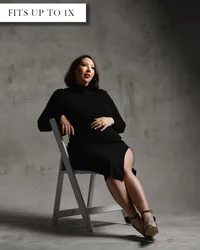 Fitted black maternity dress with a high neckline, long sleeves, and thigh-high slit revealing one leg.