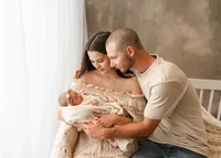 Parents leaning close and admiring their newborn in a cream blanket during a relaxed lifestyle studio session.