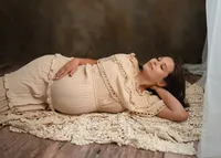 Pregnant woman reclining on a cream textured blanket, with one hand on her belly and the other beneath her head.