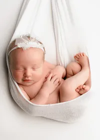 Newborn girl wearing a white floral headband, curled inside a neutral color swaddle wrap.