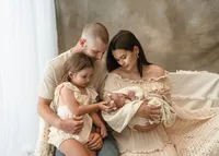 Parents and their older daughter admiring their newborn together during an unposed family moment in the studio.