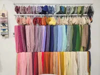 Newborn photography wraps, bonnets, and small outfits arranged by color on wall-mounted racks.