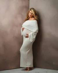pregnant mother looks down at her belly wearing a fitted cream gown with flowing sleeves against a warm neutral backdrop.