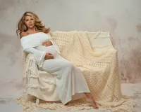 Expectant mother reclining in a fitted cream gown on a chair draped with knitted blankets for a soft studio portrait.