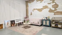 Photography studio interior with white curtains, a pink sofa, textured walls, and an open shooting area.