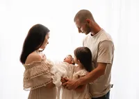 Parents standing close with their daughter and newborn beside a bright window during a relaxed family newborn portrait.