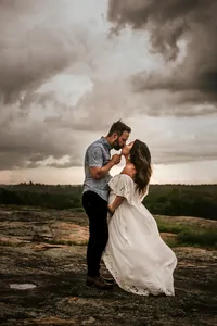pregnant woman kissing her husband romantically on a rocky overlook beneath a cloudy sky at Arabia Mountain in Atlanta.