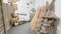 Ruffled maternity gowns beside a full-length mirror, folding screen, and dried floral arrangement.