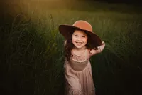 Smiling girl looking up in a pink dress and brown wide-brimmed hat during a playful outdoor portrait in golden light.
