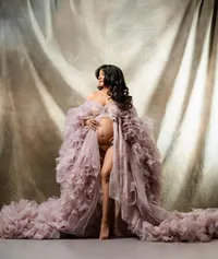 pregnant woman wearing a soft flowing mauve tulle robe against a draped cream backdrop.