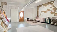 Studio seating area with a pink tufted sofa, white bench, round coffee table, and patterned rug.