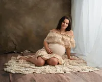 Pregnant woman smiling while seated on a cream textured blanket in a ruffled gown during a relaxed maternity session.