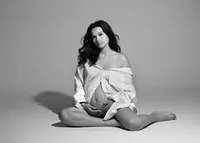 Black-and-white maternity portrait of a woman holding her belly with studio lighting and backdrop.