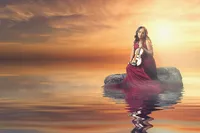 Teen sitting on rock in lake with violin getting senior portrait taken by Megan Engeseth