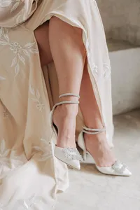 Elegant footwear and dress detail: a close-up of a person's adorned white shoes and lower hem of a flowery dress.