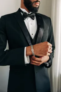A man in a black tuxedo adjusting his cufflink.