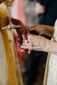 A close-up of a young woman's hand with henna tattoos touching an elderly woman's hand during a cultural event.