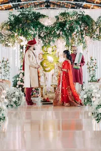 A couple dressed in traditional indian wedding attire participating in a ceremony with a celebrant.