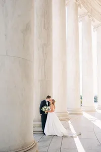 A couple in wedding attire sharing a moment among classical columns.