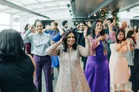 Women dancing at an indoor celebration, dressed in colorful attire, with others in the background also participating in the dance.