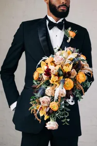 Man in a black suit holding a large floral bouquet.