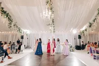 Elegant wedding reception in a decorated tent with guests seated and women in colorful dresses performing a dance.