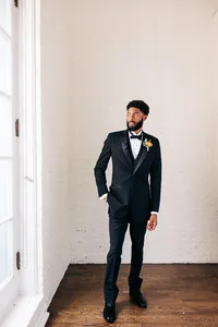 Man in a black suit standing by a window.