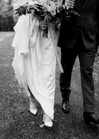 Bride and groom walking together, the focus is on their clasped hands and the bride's bouquet.