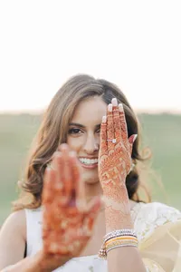 A woman showcasing her henna-adorned hands while smiling.