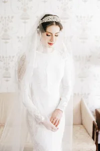 A bride in a white dress and veil with a tiara, looking down gently.