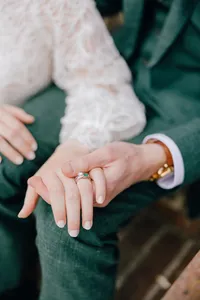 A close-up of a person's hand with a ring on the ring finger, resting on another person's leg, suggesting a moment of affection or connection.