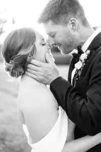 A black and white photo of a smiling couple in wedding attire embracing and gazing affectionately at each other.