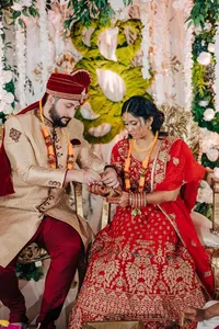 Bride and groom in traditional indian wedding attire performing a ritual at their ceremony, surrounded by floral decorations.