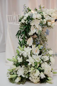 Elegant floral arrangement with white lilies, hydrangeas, and other greenery on a draped table at an event.