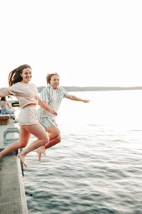 a couple hold hands as they jump off the dock into the water.