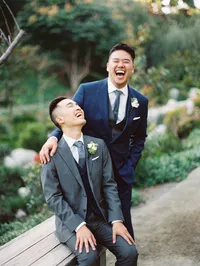 Two grooms, one sitting, and the other standing, laughing out loud at the Japanese Friendship Garden in Balboa Park