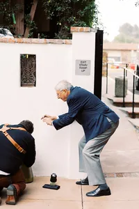 photographer with cross back strap photographs some rings on the ground, next to him is a grandfather squatting holding an iphone trying to get the same photo