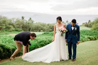 wedding photographer wearnig a black shirt and khakis fixes a brides dress