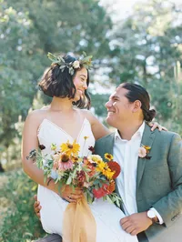 bride and groom look at eachother smiling and giggling, the bride holds a wildflower bouquet and wears a flower crown, the groom wears a daisy bouttoniere at Pine Hill in Julian