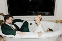 Bride and groom sharing a playful moment in a clawfoot bathtub during their Holland, Michigan wedding celebration.