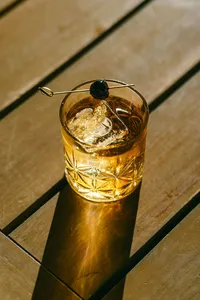 Old fashioned with a cherry garnish in a cut-crystal glass casting a golden shadow across a wooden table, cocktail photography for a luxury hotel
