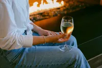 Guest holding a glass of white wine beside the outdoor fire feature