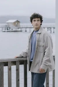 Model in an oatmeal fleece overshirt over a blue tee with straight denim, at the dock railing