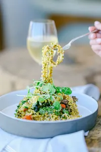 Plated pasta with greens and a glass of white wine, boutique hotel food photography