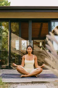 Woman meditating on a yoga mat outside a mid-century modern home, wellness brand lifestyle photography