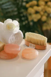 Rolled spa towel with a gardenia, a dry body brush, and pink Himalayan salt stones set for a treatment at Spa L’Auberge, hotel spa detail photography