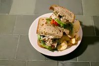 Natural Catch albacore sandwich on sourdough with red pepper, avocado, and butter lettuce, served with chips on green tile
